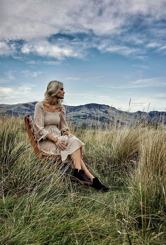 A person sitting in a field with mountains in the background. Wearing glerups boots in Charcoal grey. 