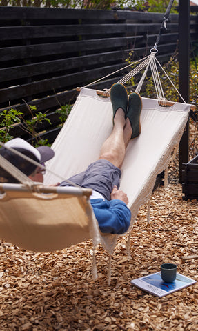 A person relaxing in a hammock outdoors while wearing glerups shoes in the color Forest green with natural rubber soles. 