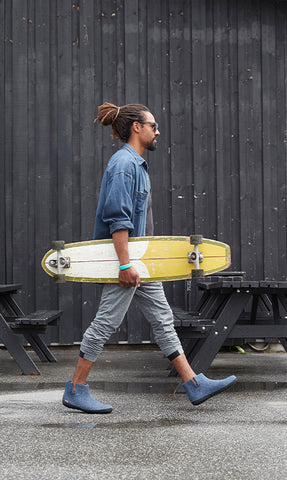A person walking with a skateboard while wearing glerups boots in the color Denim with black rubber soles.