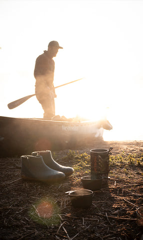 glerups boots in the color Denim blue with natural rubber soles placed outdoors next to outdoor gear. 