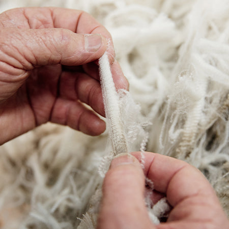 Hands working with raw wool fibers during production
