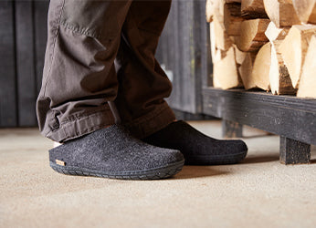 Close up picture of two feet wearing glerups slip-ons in the color Charcoal grey with natural rubber soles in black. 