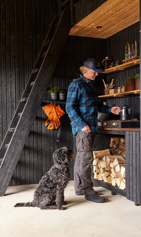 A person standing in an outdoor kitchen. Behind the person is a dog. 