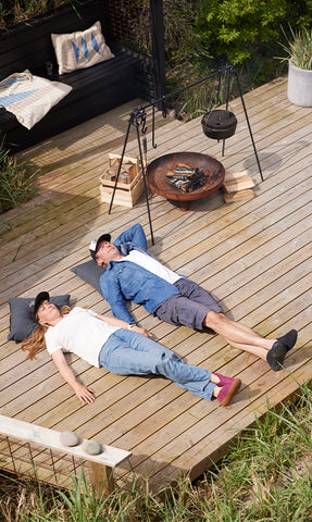 Two people relax on a wooden deck beside an outdoor fire pit, wearing glerups slippers while enjoying a quiet moment together.